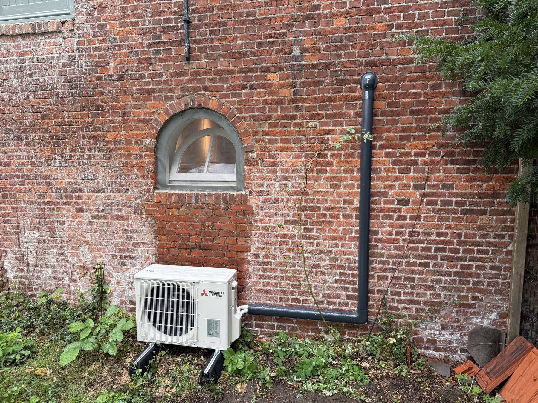 Buitenunit met leidingwerk tegen een historische bakstenen gevel