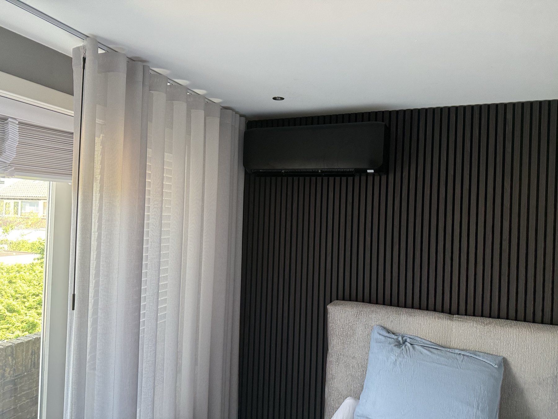 Zwarte airco geïntegreerd tegen een donkere houten lattenwand